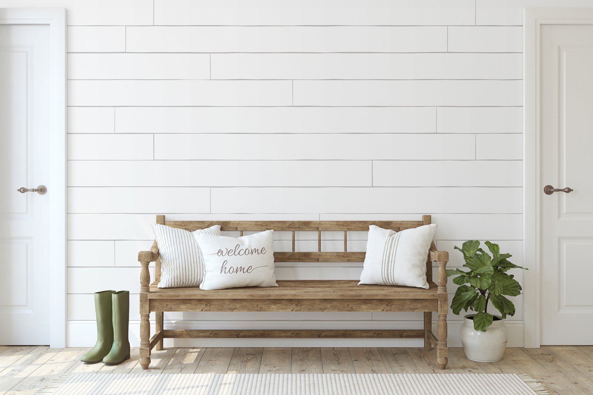 Rustic wooden bench with two decorative pillows, a potted plant, and green rain boots. The backdrop features a simple, white shiplap wall, enhancing a welcoming entryway atmosphere.